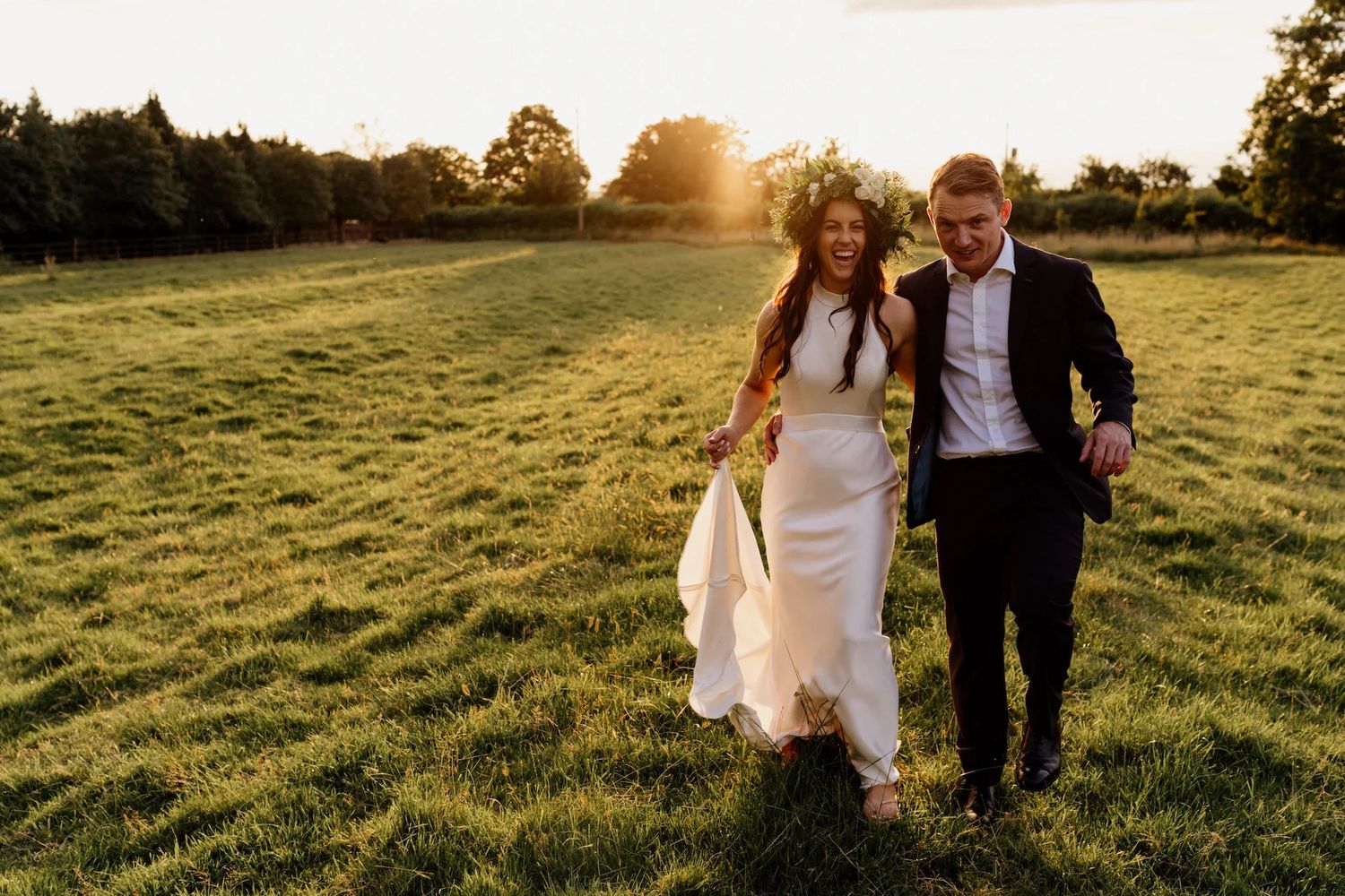 Happy couple walking together through a sunlit meadow at golden hour during their wedding.