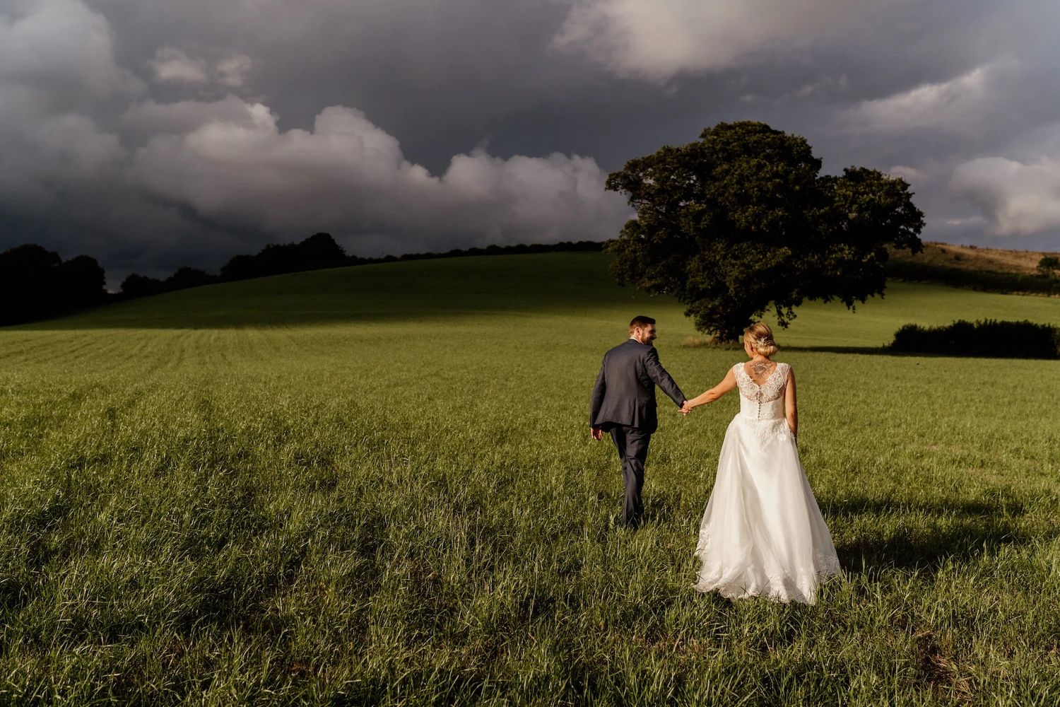 Wedding couple walking through dramatic stormy field under dark clouds.