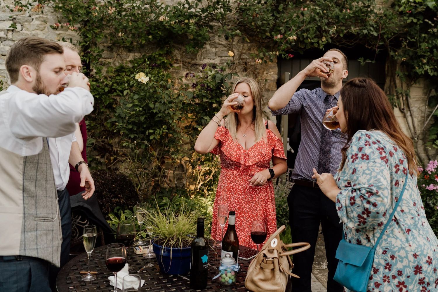 People mingling and sharing drinks at a casual outdoor celebration with natural greenery.