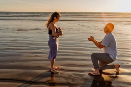 Two figures silhouetted against a sunset on a beach during a romantic moment.