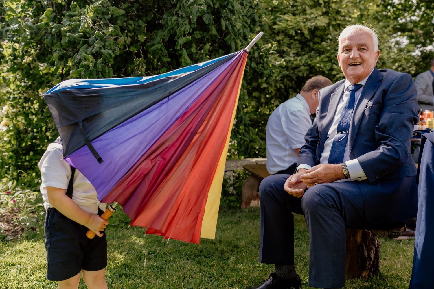 Outdoor gathering with people holding a vibrant rainbow flag in a garden setting.