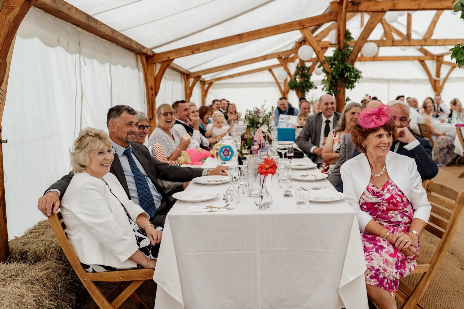 Wedding reception guests seated at long tables under a wooden beam ceiling in an elegant rustic venue.