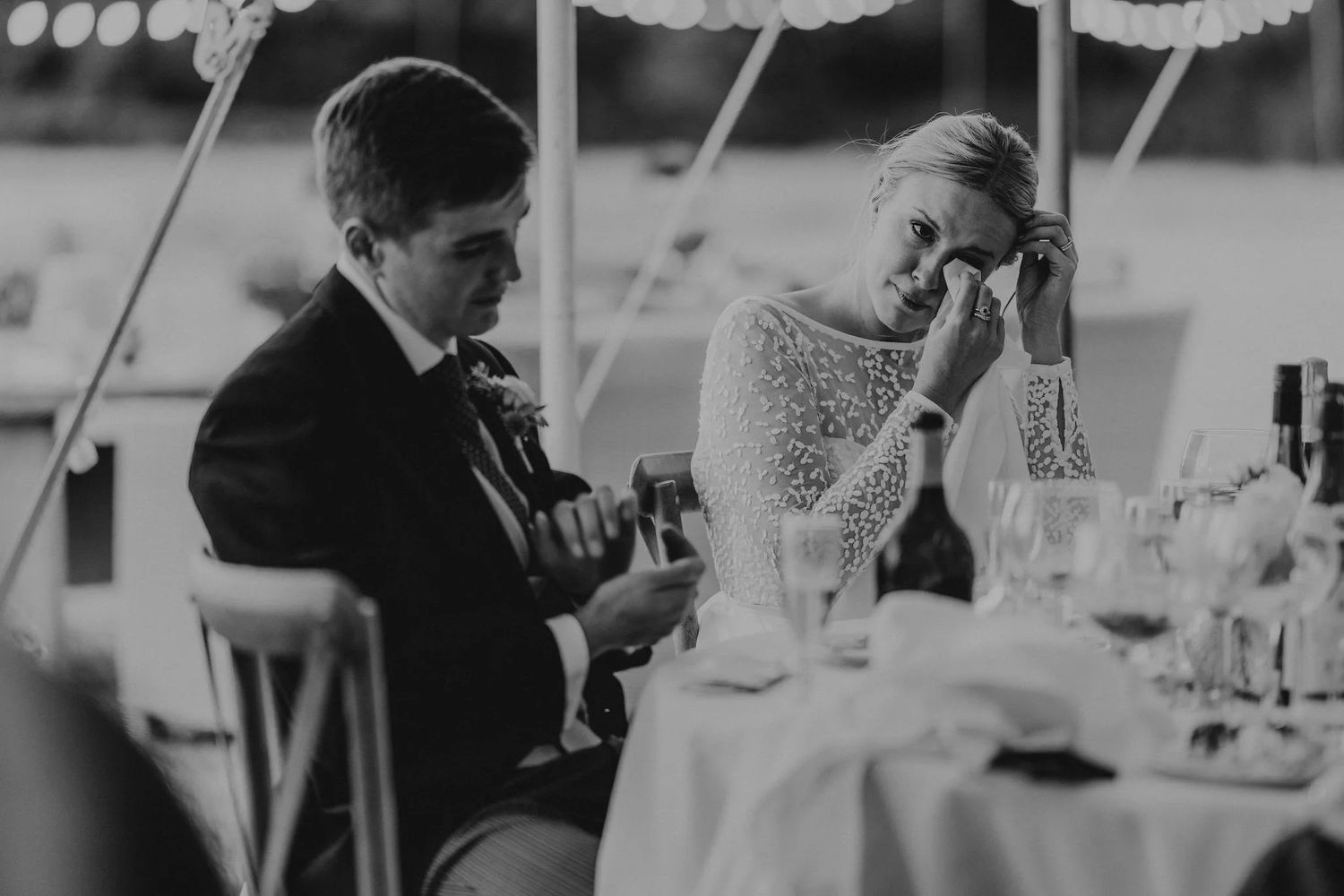 Wedding reception scene with table settings and glassware in black and white.