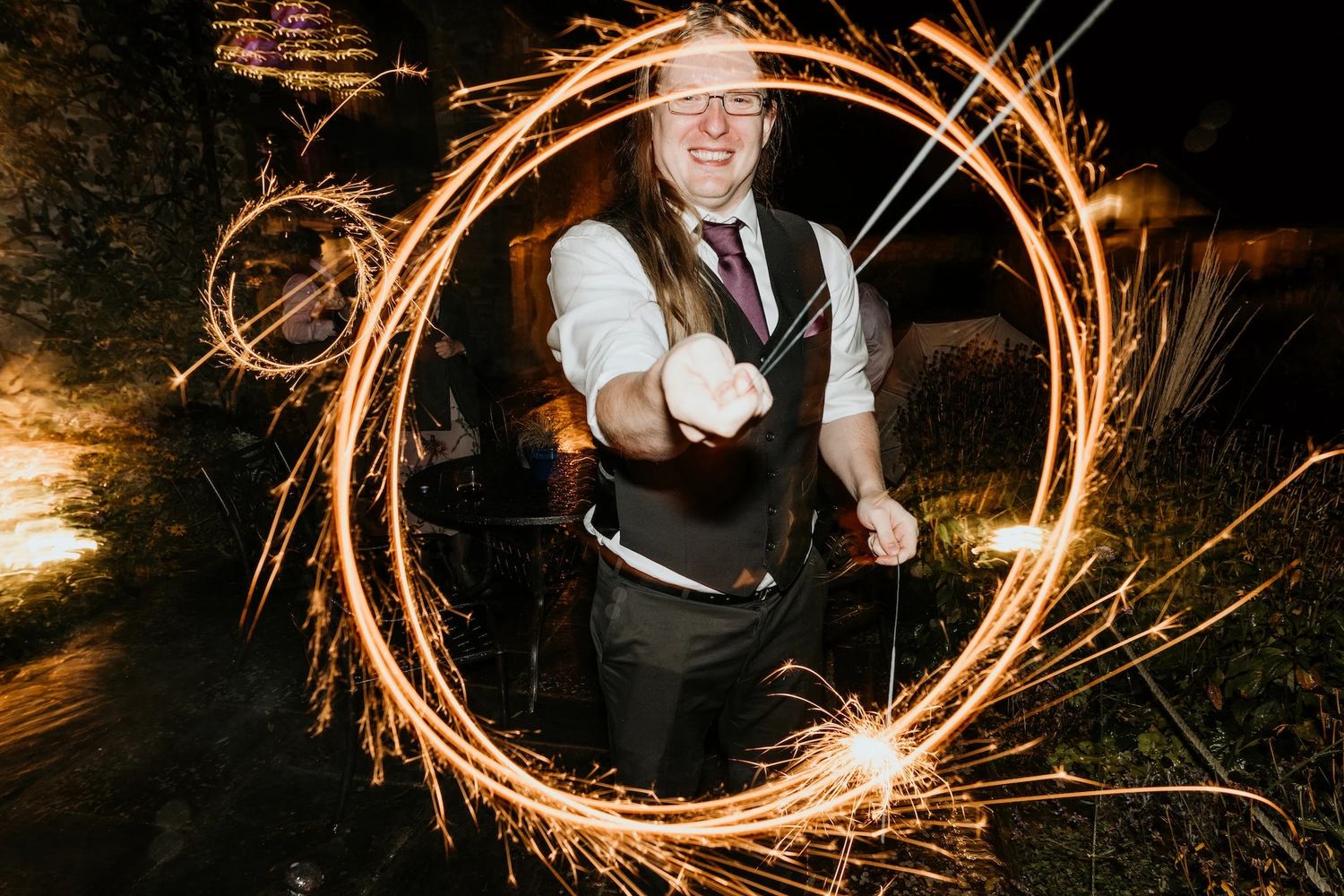 Sparklers create glowing circles of light during nighttime wedding photo session.