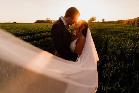 Wedding couple in golden sunset light with flowing dress in a field.