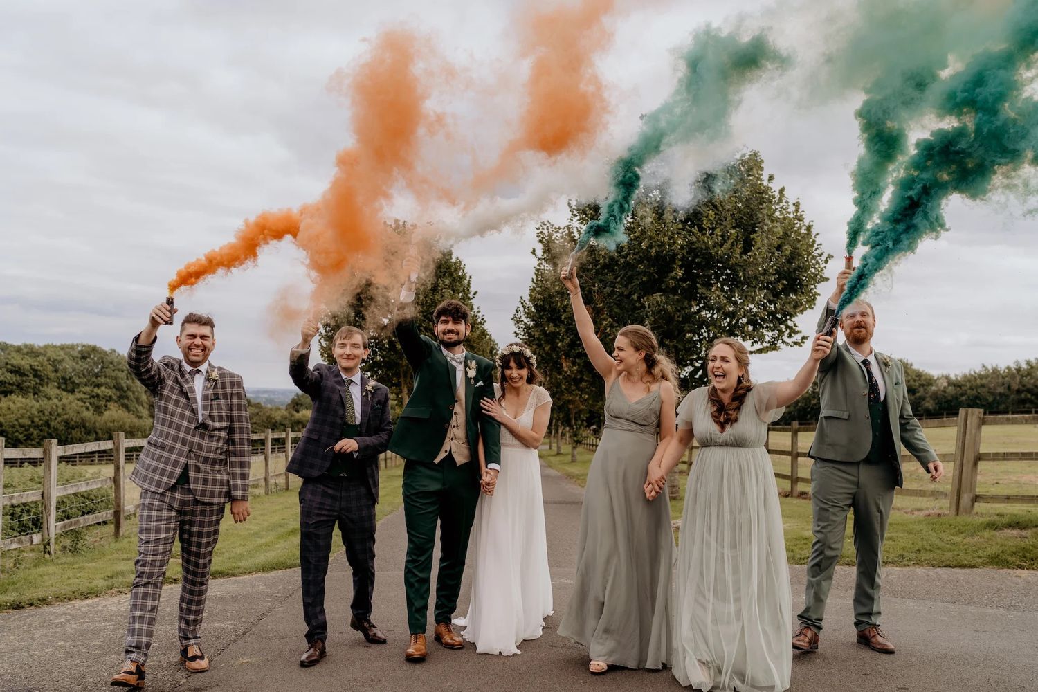 Wedding party celebrating with colorful smoke bombs on a country road.