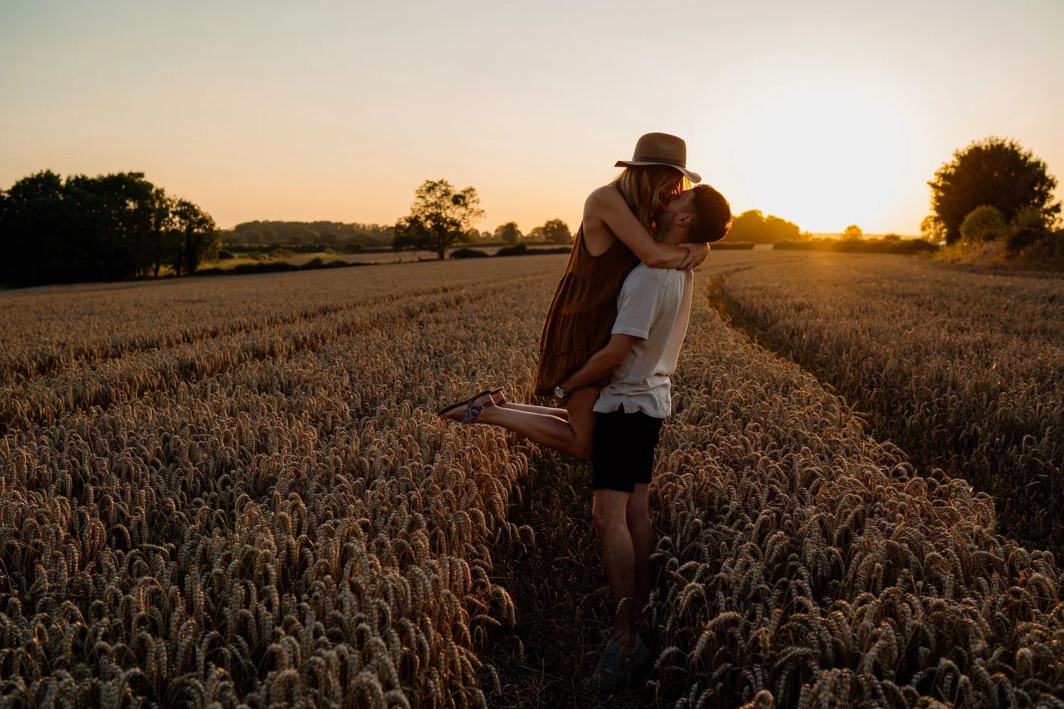 Dreamy sunset engagement photos in a rustic wheat field with golden light filtering through the scene.
