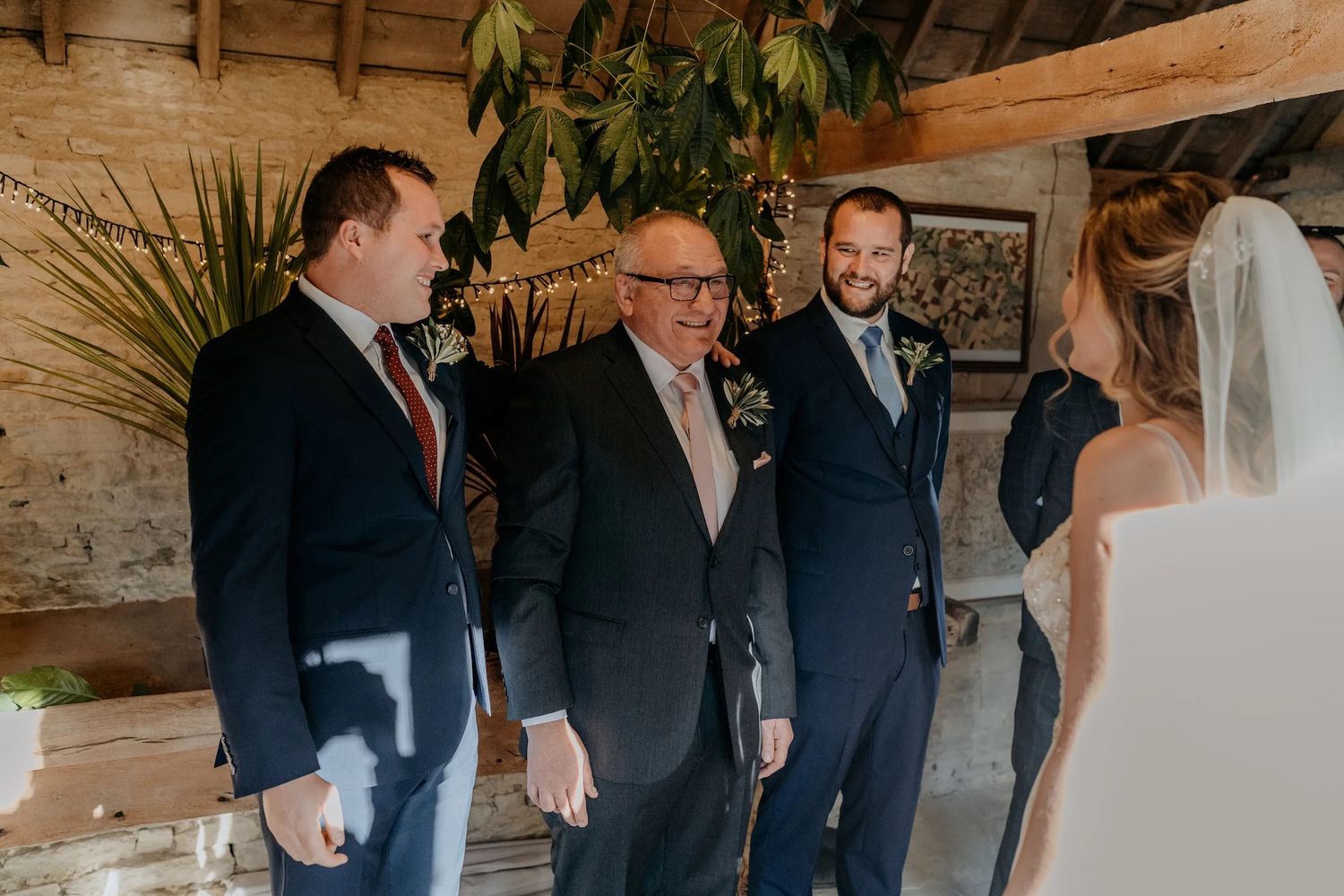 Wedding party standing inside rustic wooden venue with natural lighting.