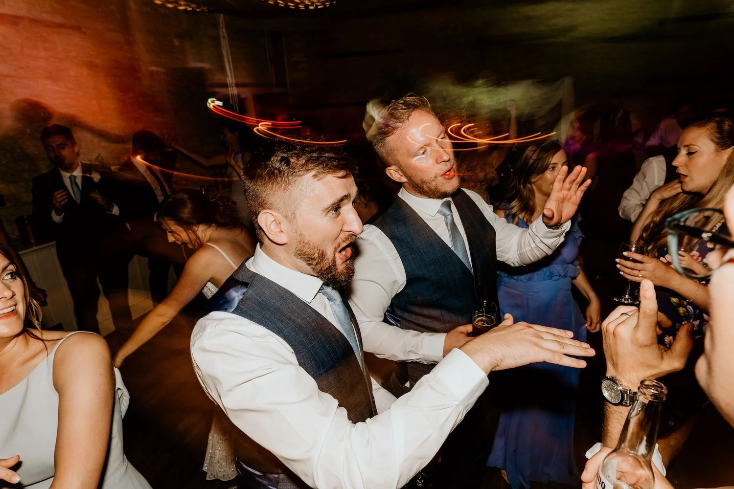 Wedding guests dancing and celebrating on a dimly lit dance floor at a reception.