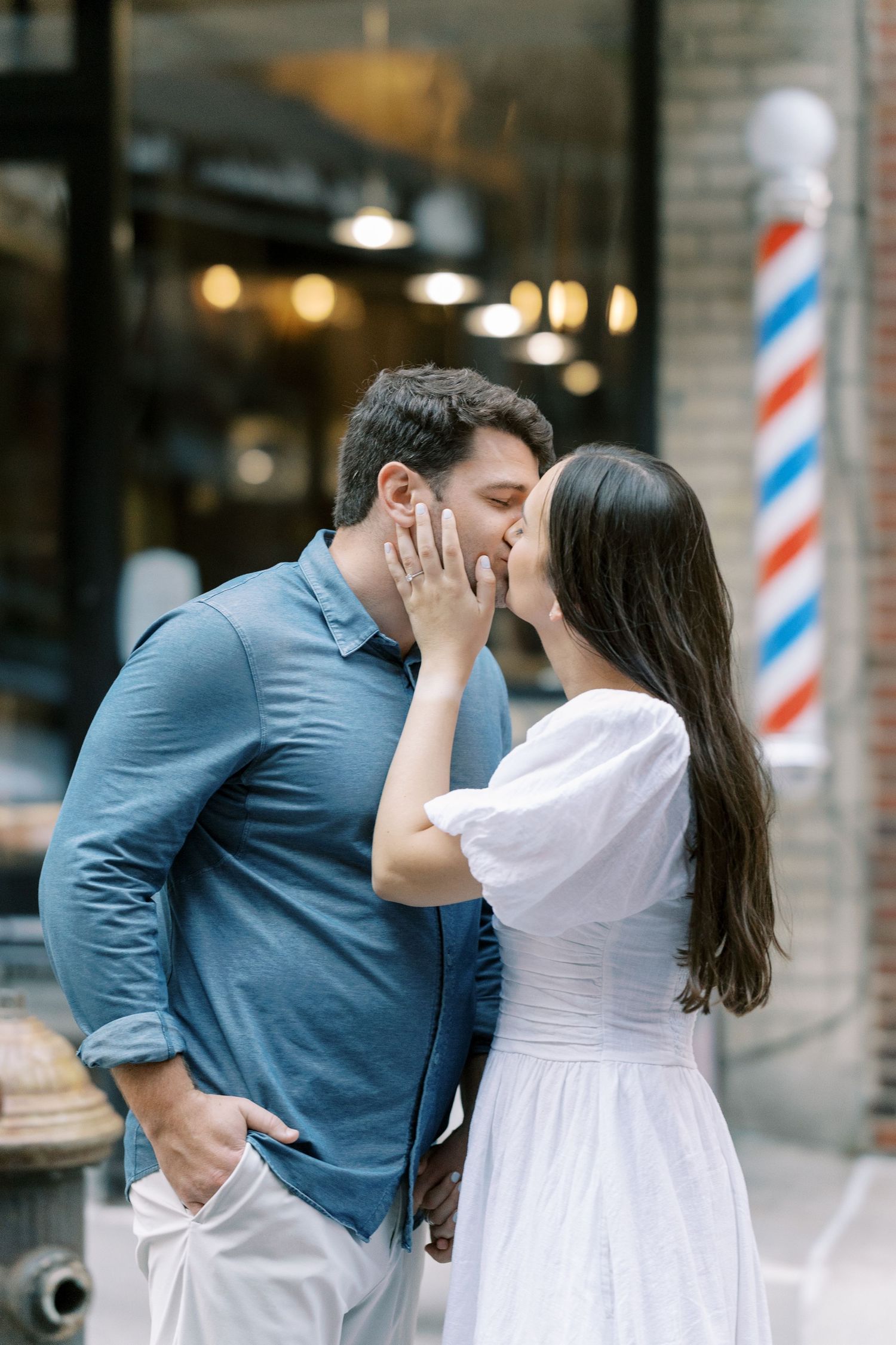 A couple in coordinating white and blue outfits share romantic kisses in a series of candid outdoor shots by a barbershop pole.