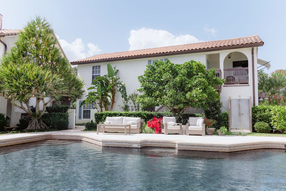 Mediterranean-style white stucco buildings with red tile roofs and pool surrounded by lush landscaping.
