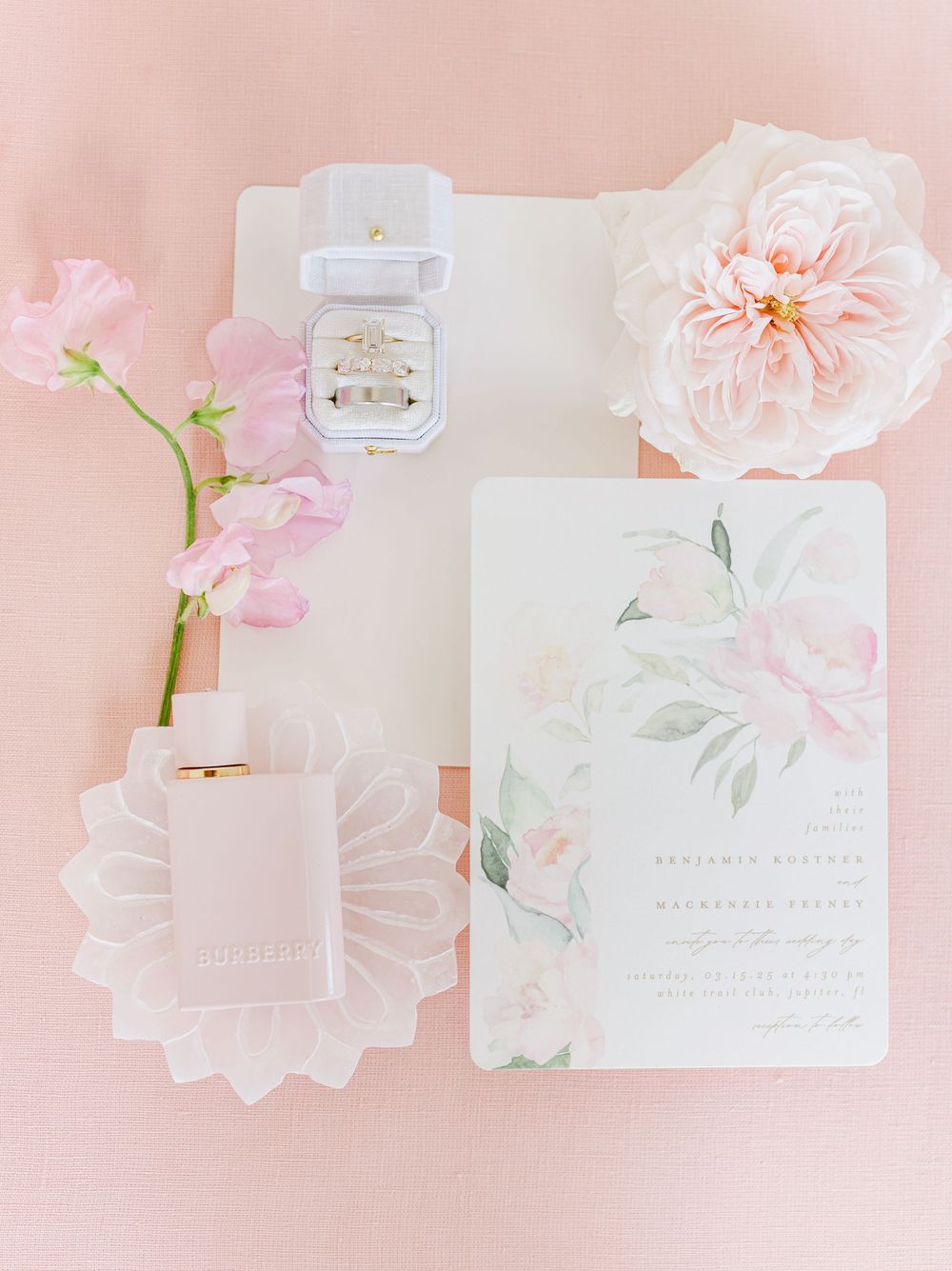 Delicate pink wedding invitation suite with floral design, rings, and sweet pea flowers on blush background.