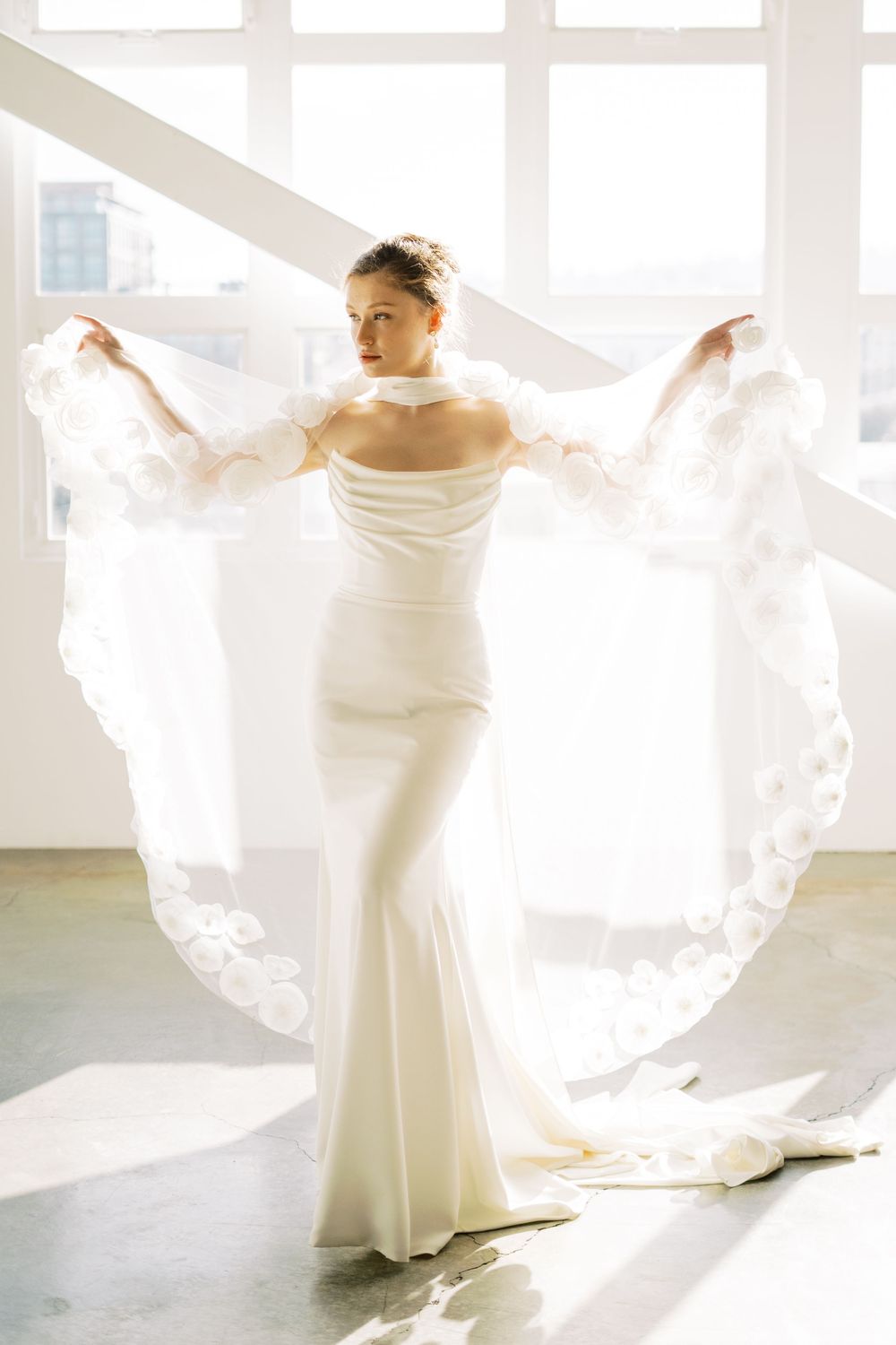 Elegant white wedding dress with flowing veil captured in bright natural window light.