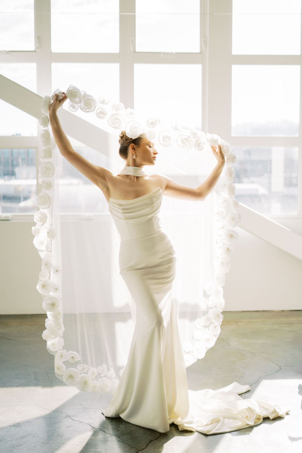 A person in a white wedding gown twirls in front of bright windows creating ethereal bridal portraits.