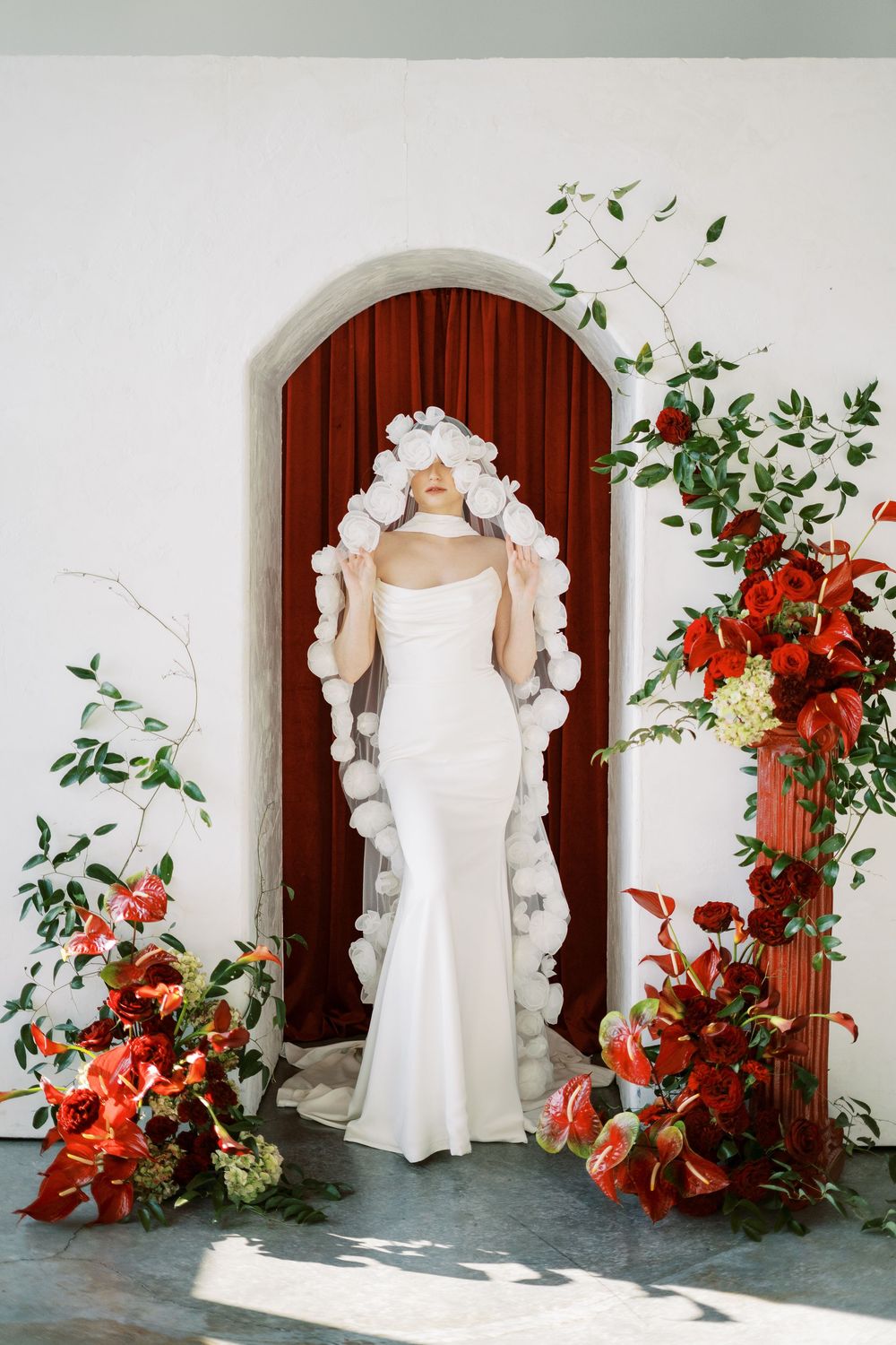 Wedding dress display with red curtains and vibrant orange floral arrangements in an elegant studio setting.