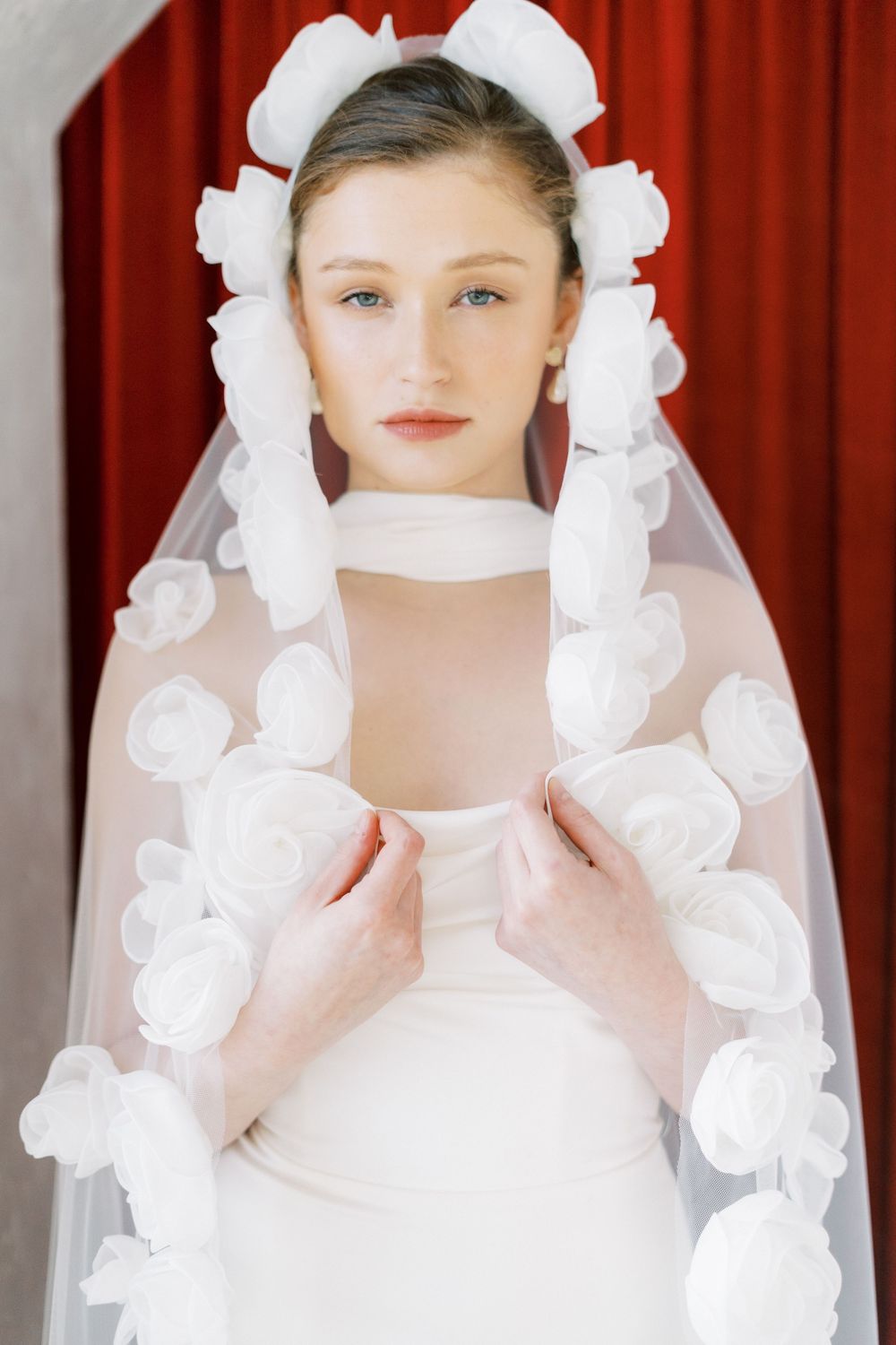 Wedding veil adorned with delicate white fabric roses frames elegant bridal portrait.