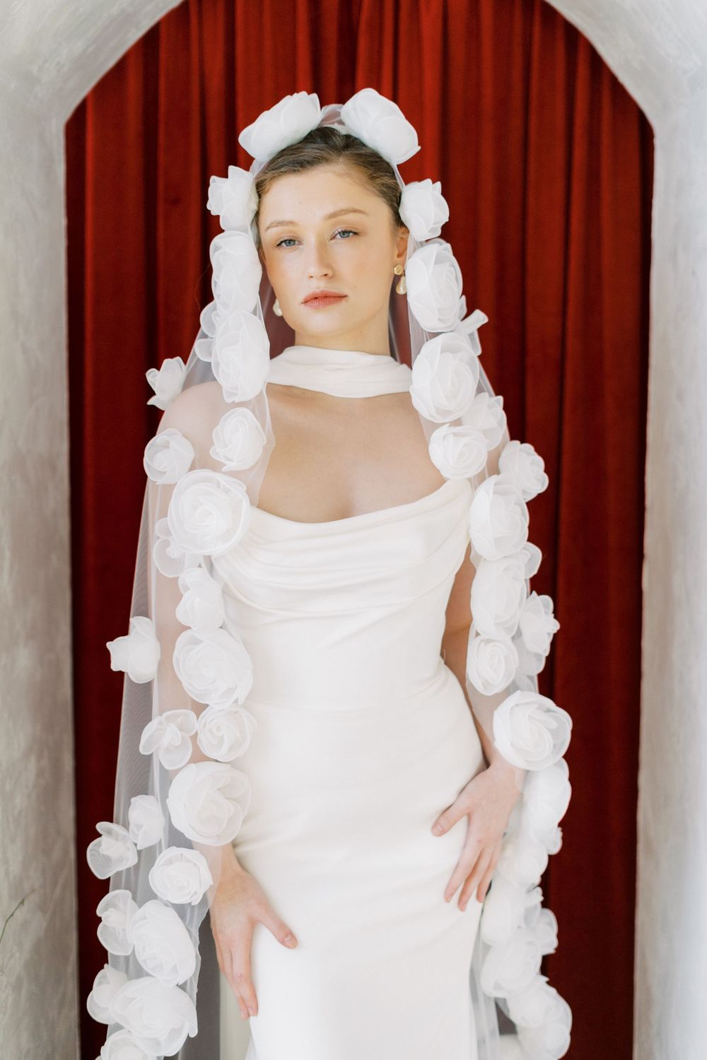 Wedding dress portrait showcasing white floral details against a red curtain backdrop.