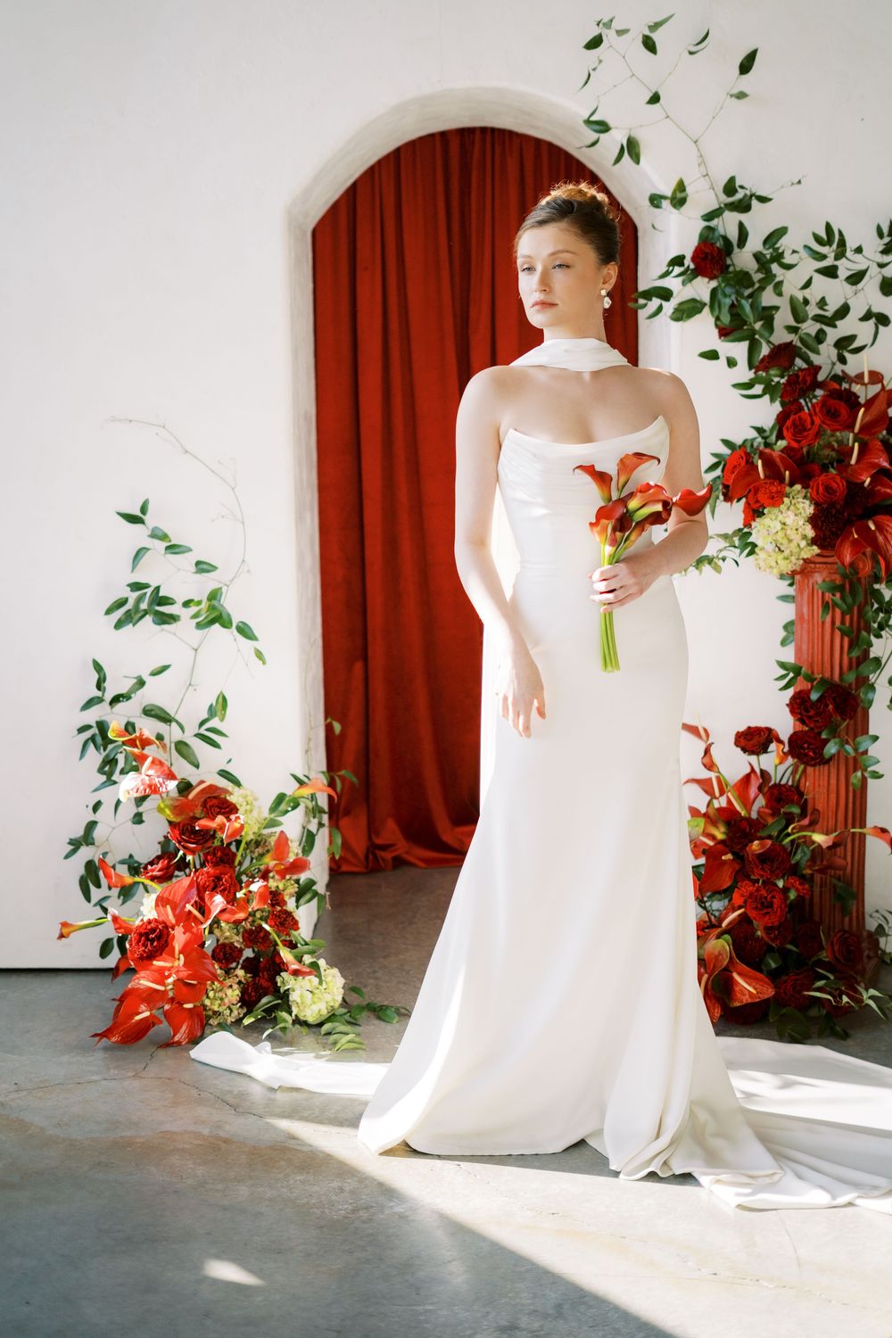 Elegant wedding dress photo with white gown and red floral arrangements against a dramatic red curtain backdrop.