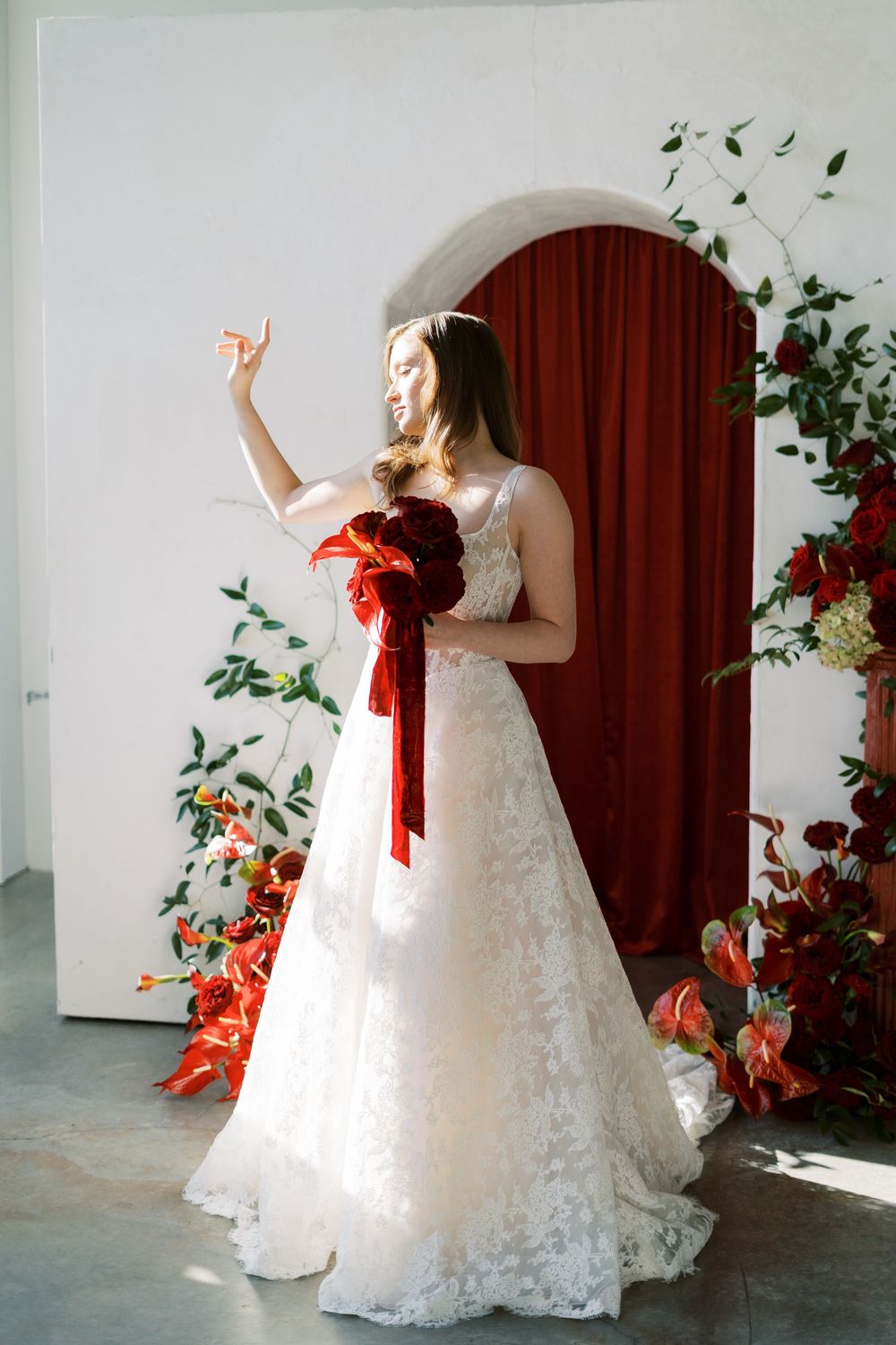 A white wedding dress photoshoot against a burgundy curtain backdrop with orange floral arrangements.