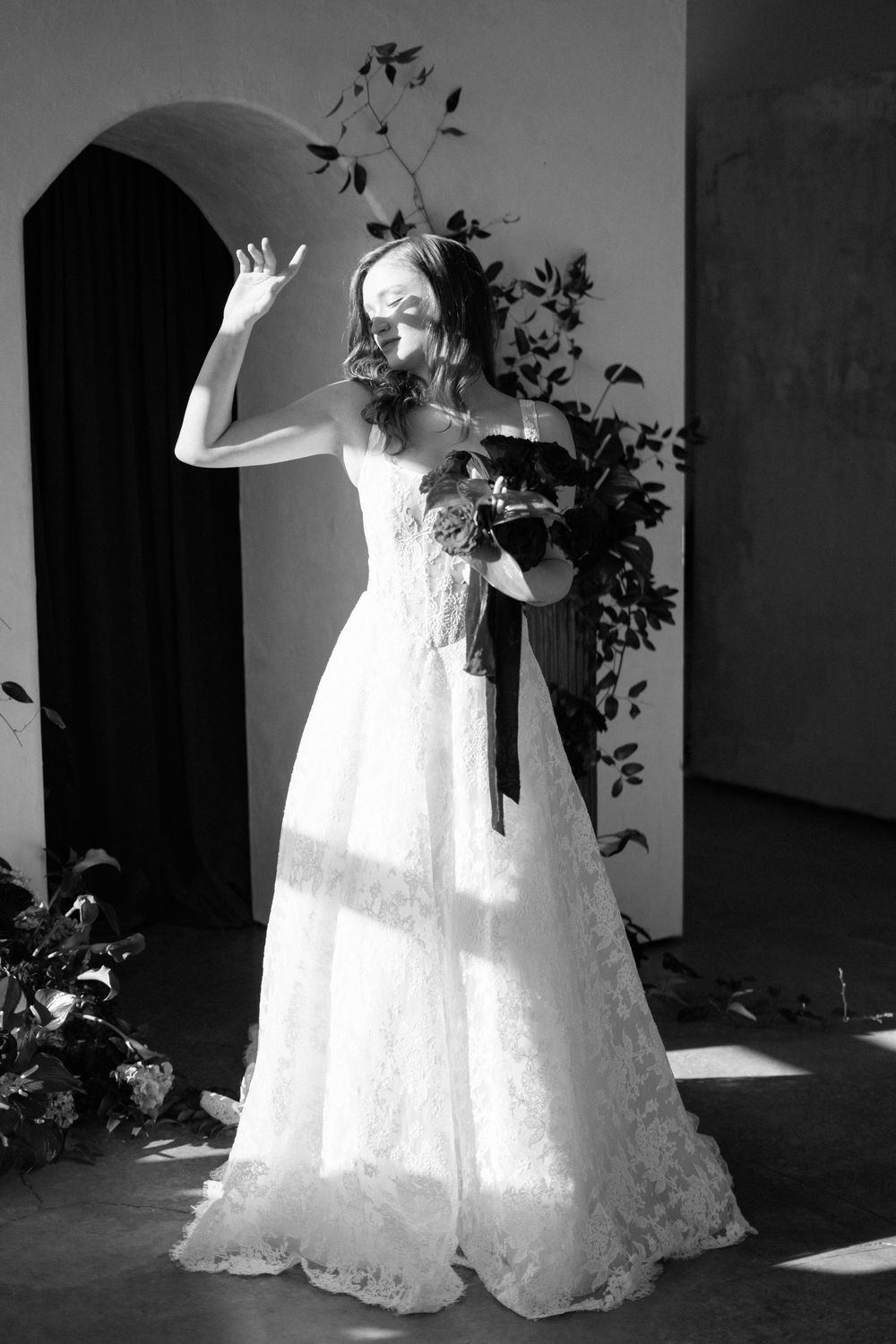 Artistic black and white photographs capture a bride in a flowing lace gown against shadows and foliage.