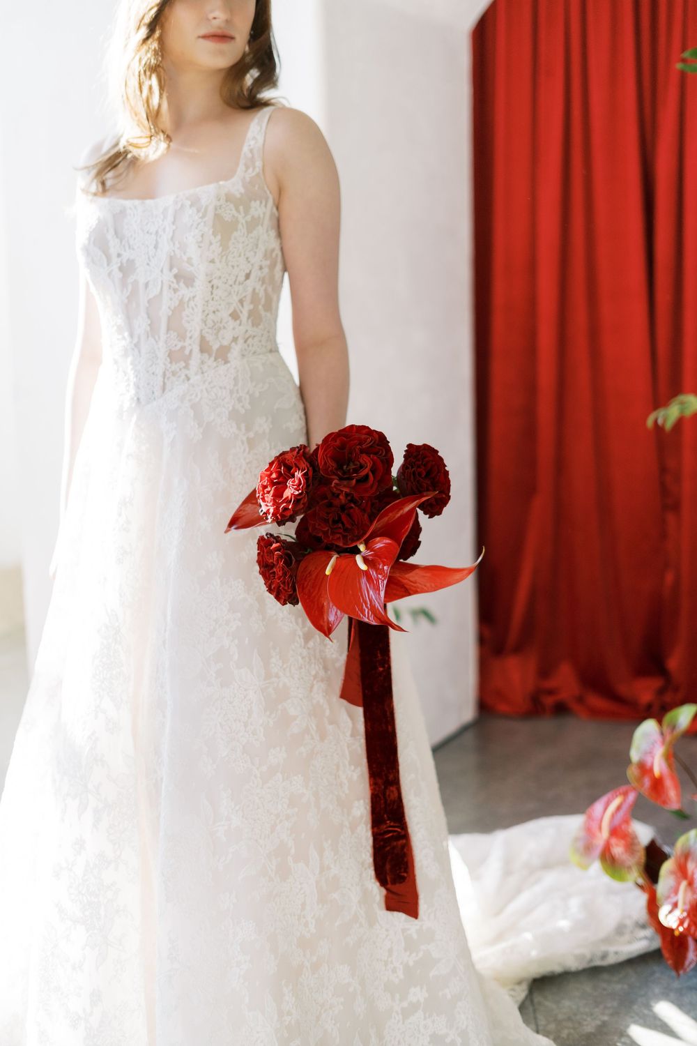 A bridal fashion series featuring a white lace dress with deep red ribbon accents against a red curtain backdrop.