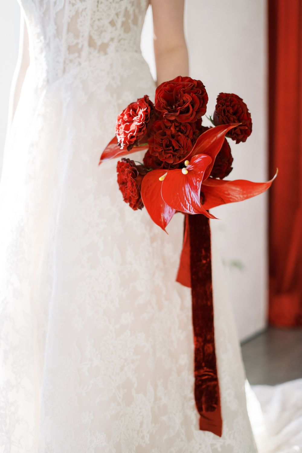 Close-up detail of red velvet roses and ribbons decorating a white bridal gown.