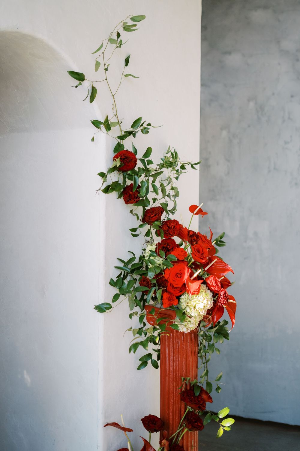 Climbing red roses and greenery arrangement decorating a white wall with elegant floral design.