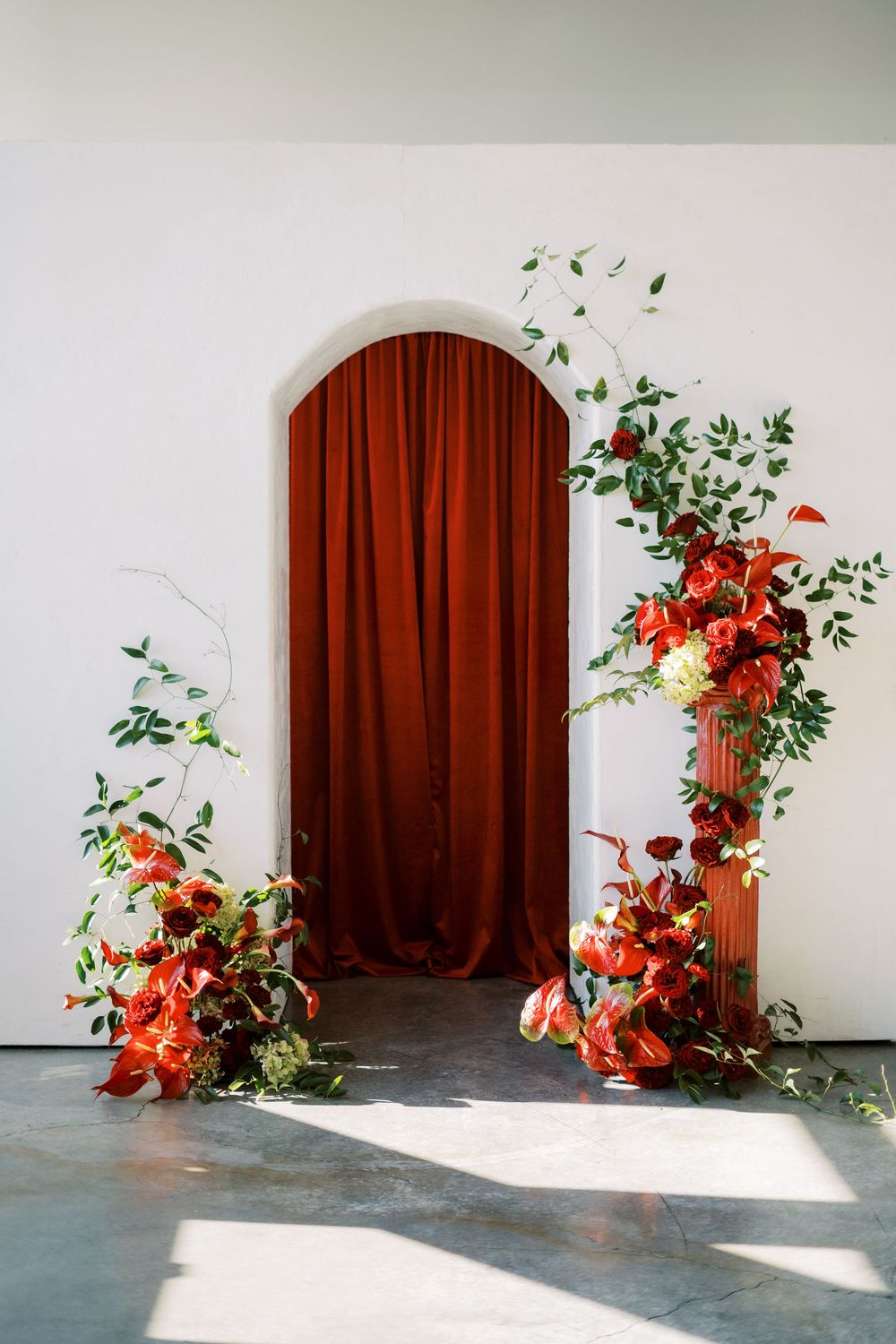Minimalist studio setup with red curtains and orange floral arrangements creating an elegant backdrop.