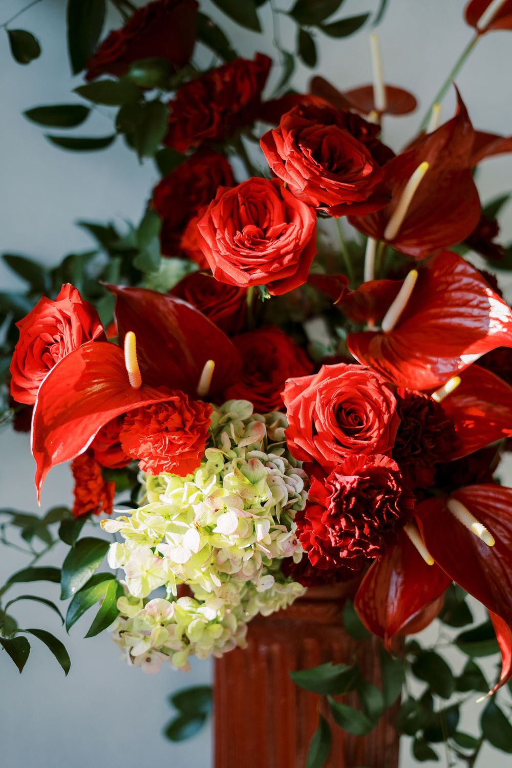 Elegant floral arrangement featuring vibrant red roses and white hydrangeas with green foliage in a wooden container.