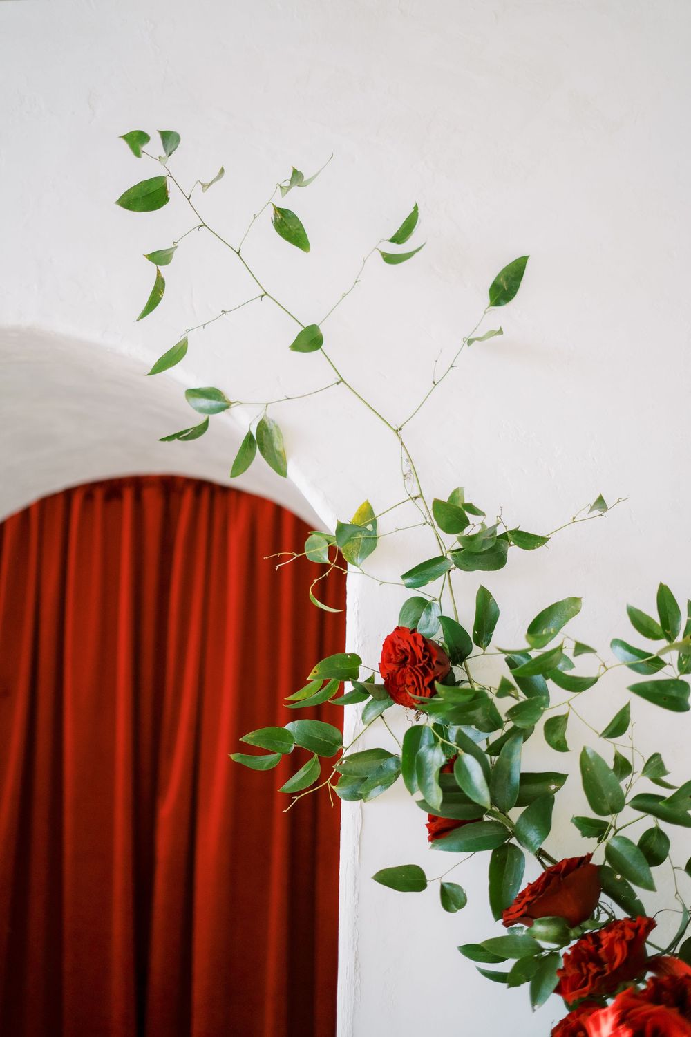 Red roses and green foliage arranged against a rustic archway with deep red curtains.