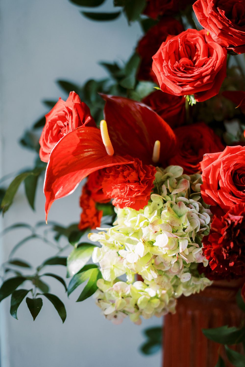 Beautiful floral arrangement featuring vibrant red roses, anthurium lilies, and white hydrangeas against a light background.