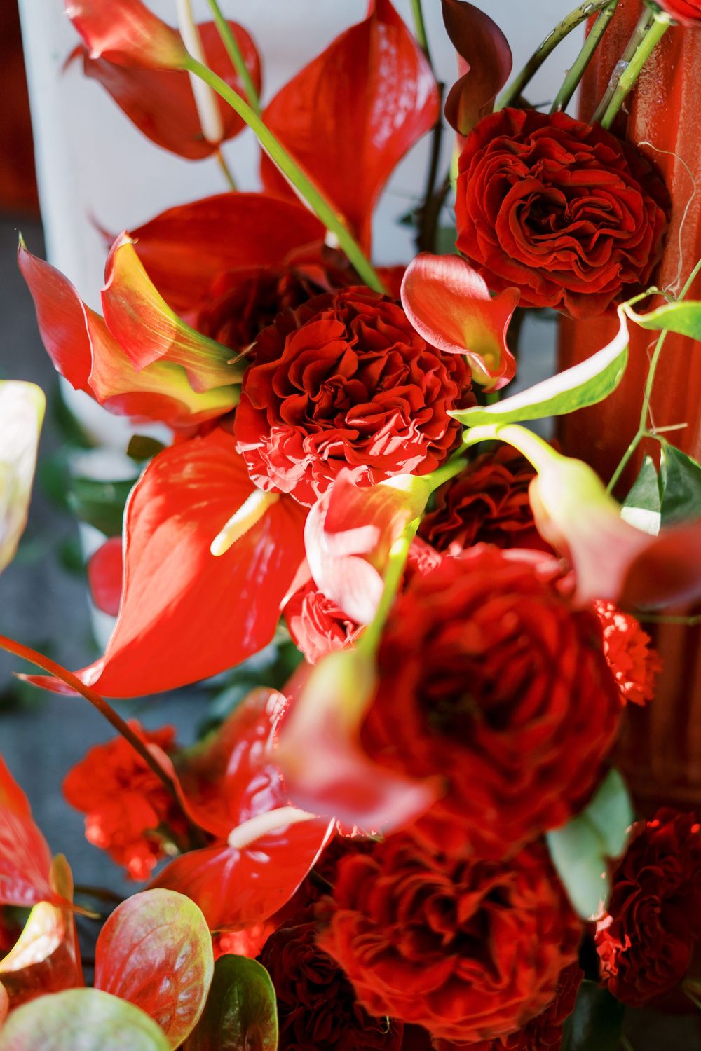 Lush red roses and calla lilies create a dramatic floral arrangement with deep crimson tones and elegant green stems.
