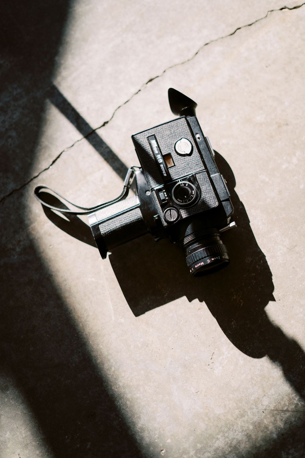 Overhead view of a black vintage camera with lens casting dramatic shadows on a light surface.
