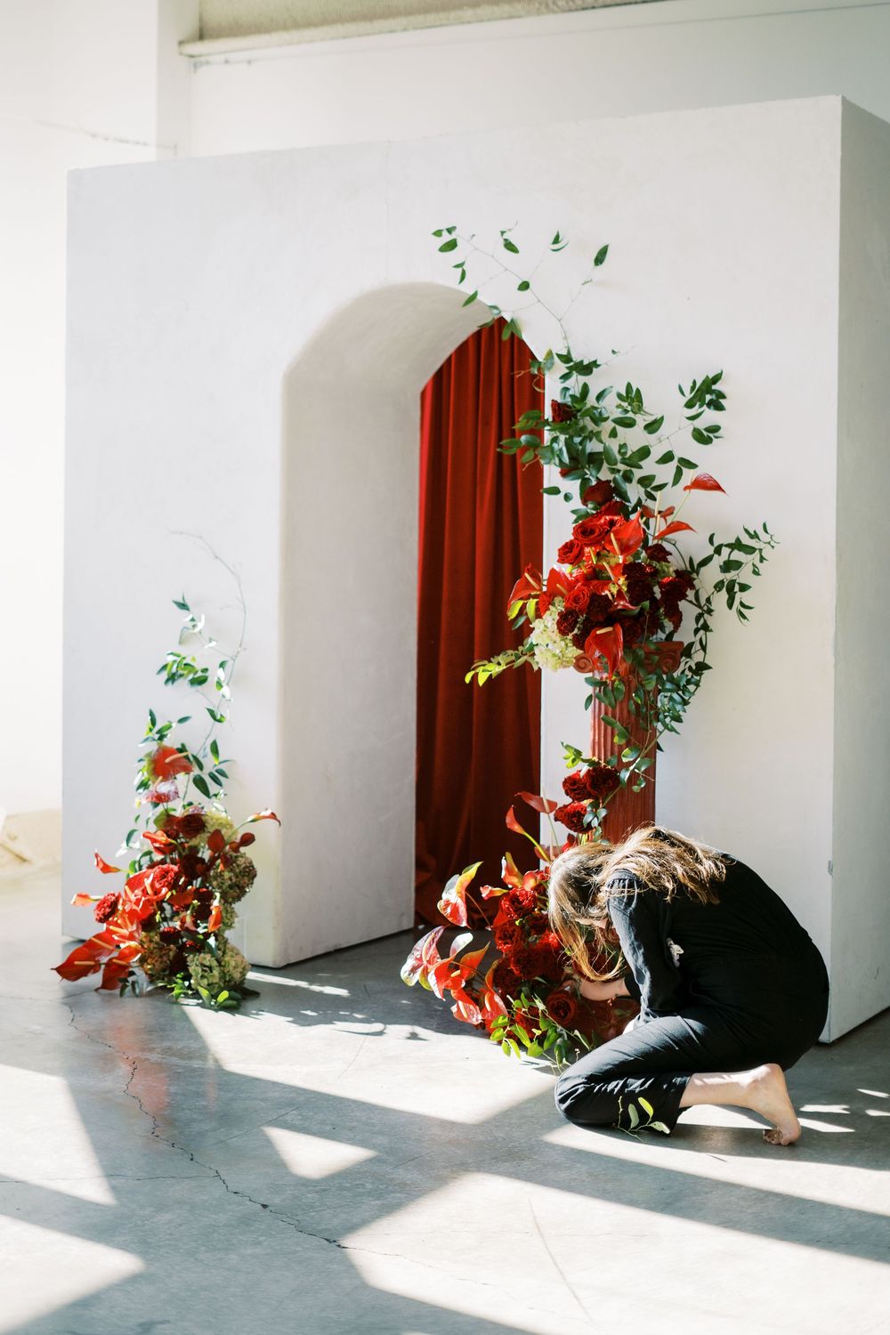 Minimalist interior space with white walls, brown door trim, and floral arrangements casting shadows.