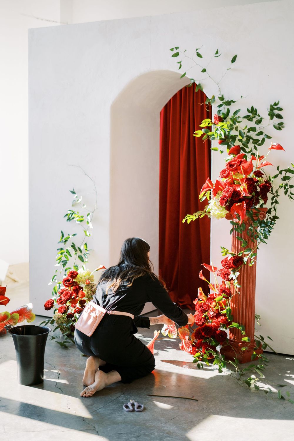 Artistic photo series showing a person in black arranging red flowers and greenery against a white wall.