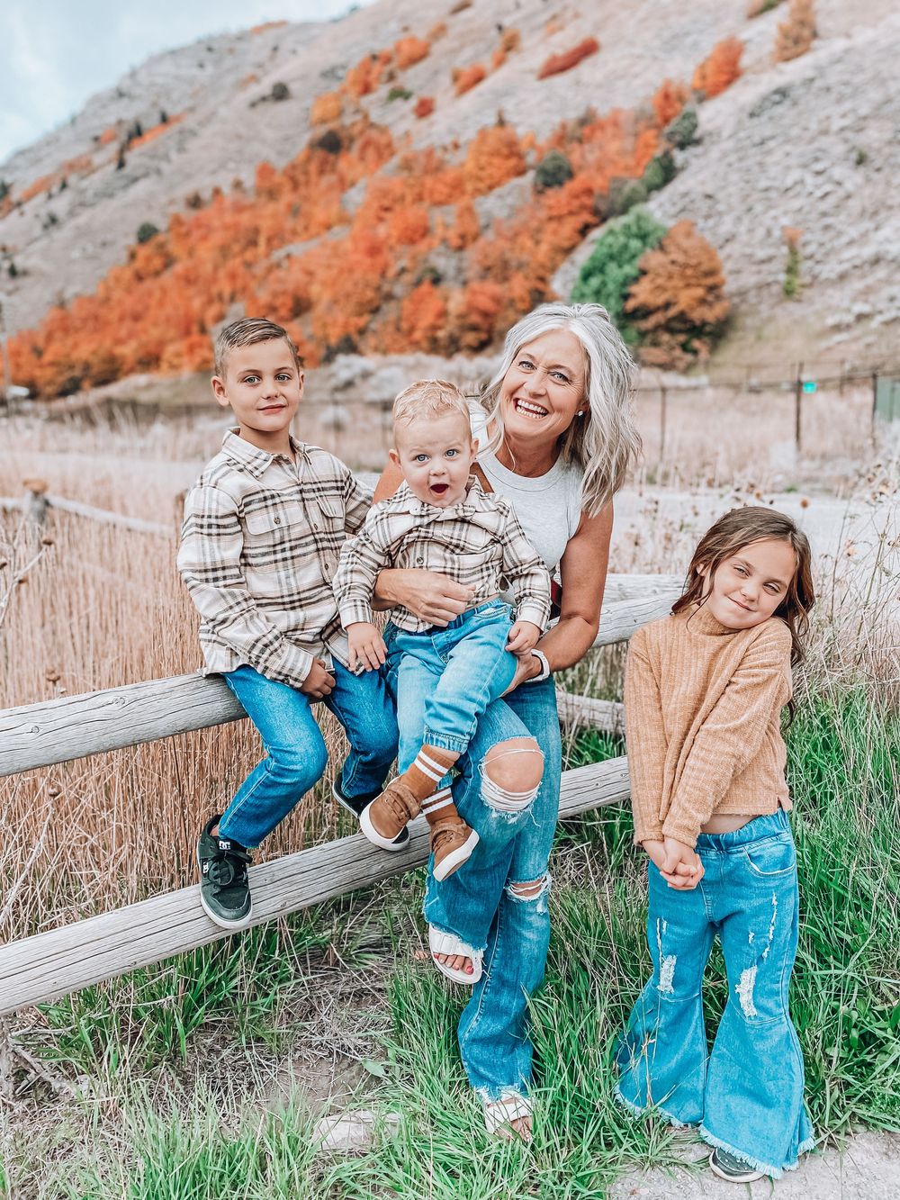 Group sits on wooden fence against autumn mountain backdrop with vibrant orange foliage.