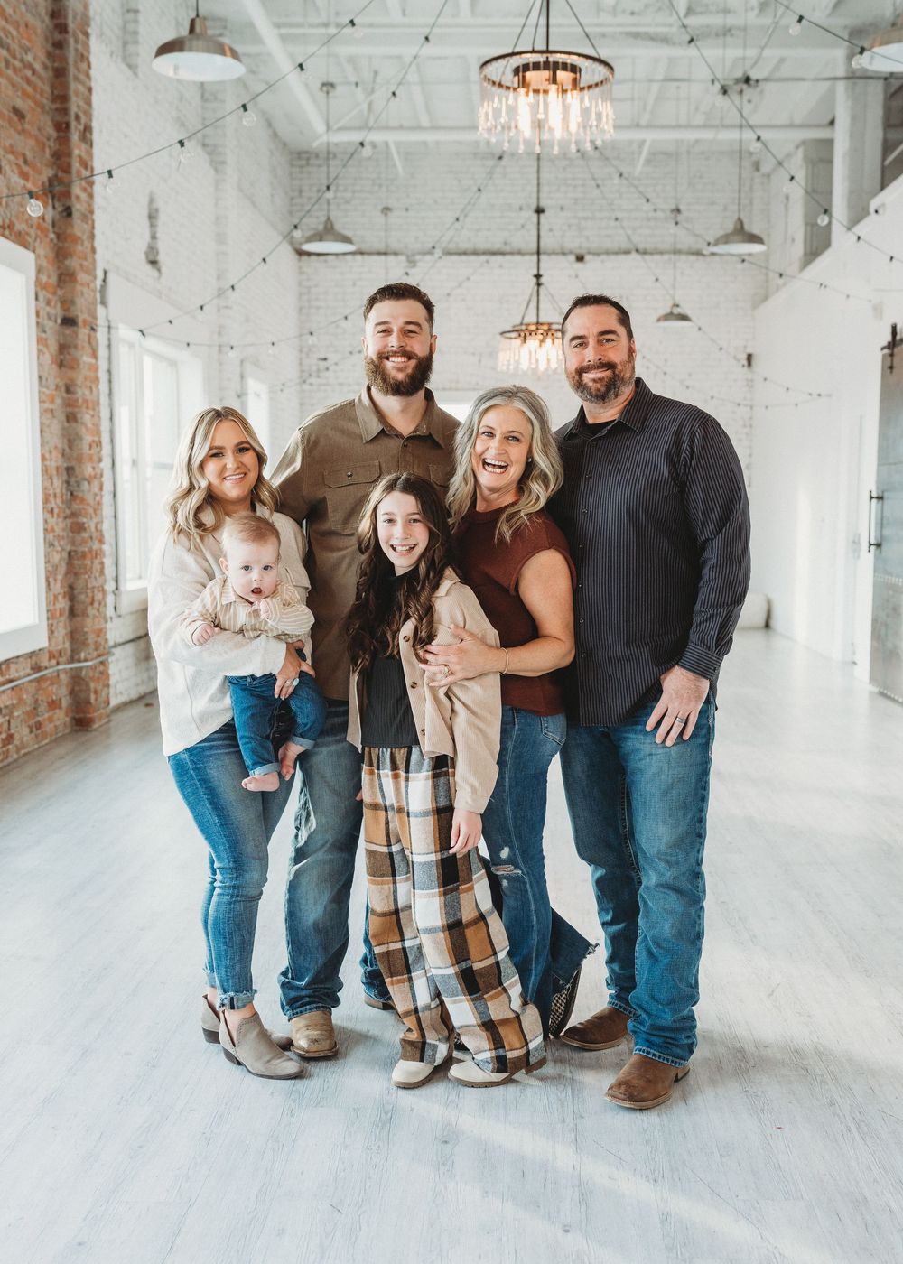 A stylish group poses together in a bright industrial space with exposed brick and crystal chandeliers.