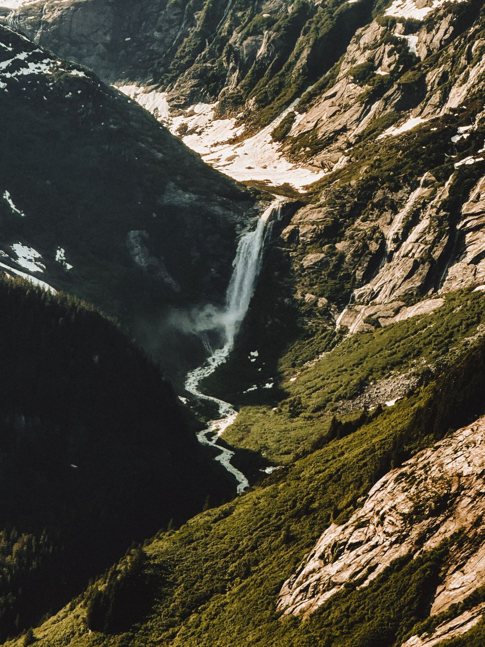 Dramatic aerial view of a waterfall cascading down steep mountain cliffs in wilderness terrain.