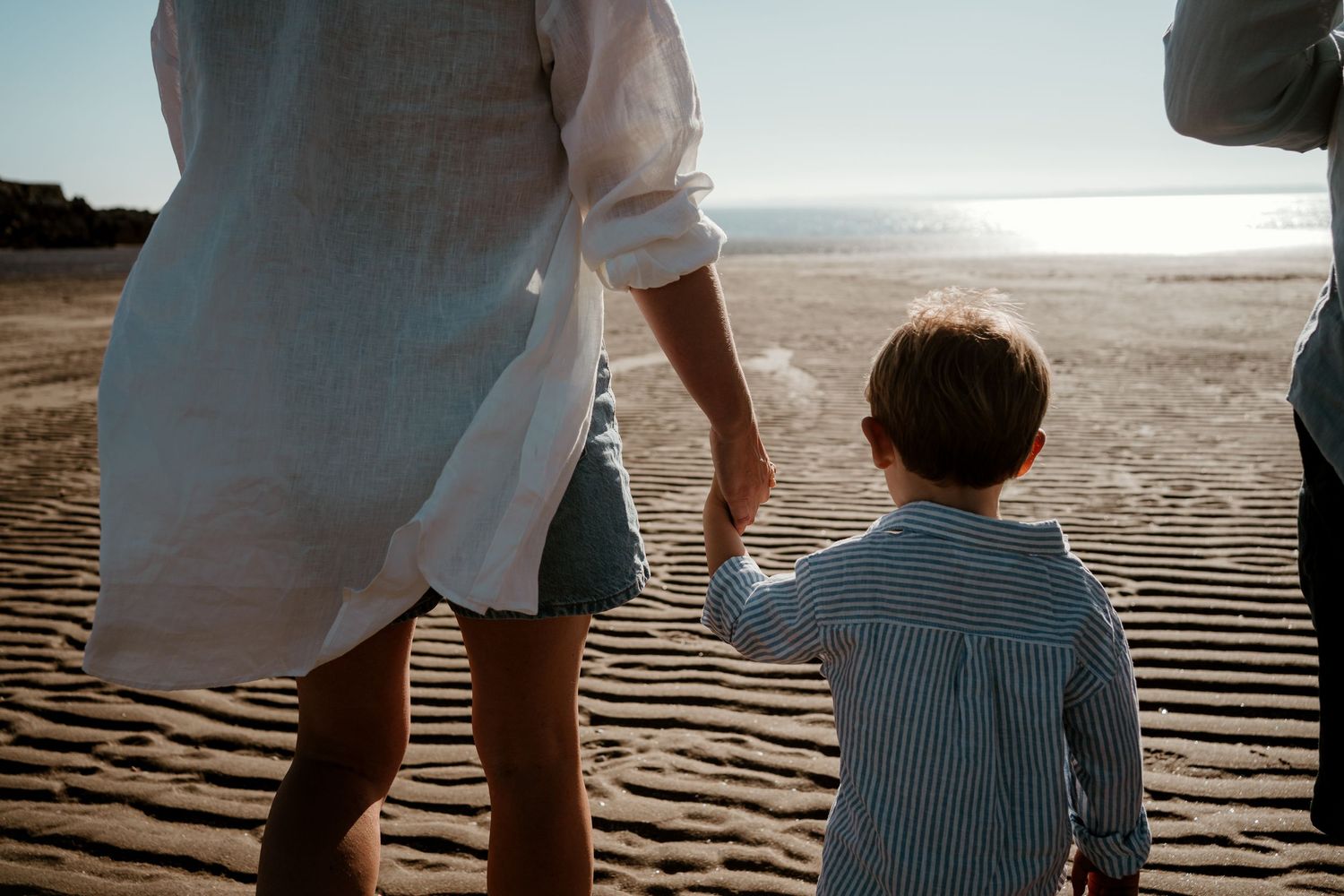 Family walking along beach shoreline during golden hour creating silhouettes against the ocean.