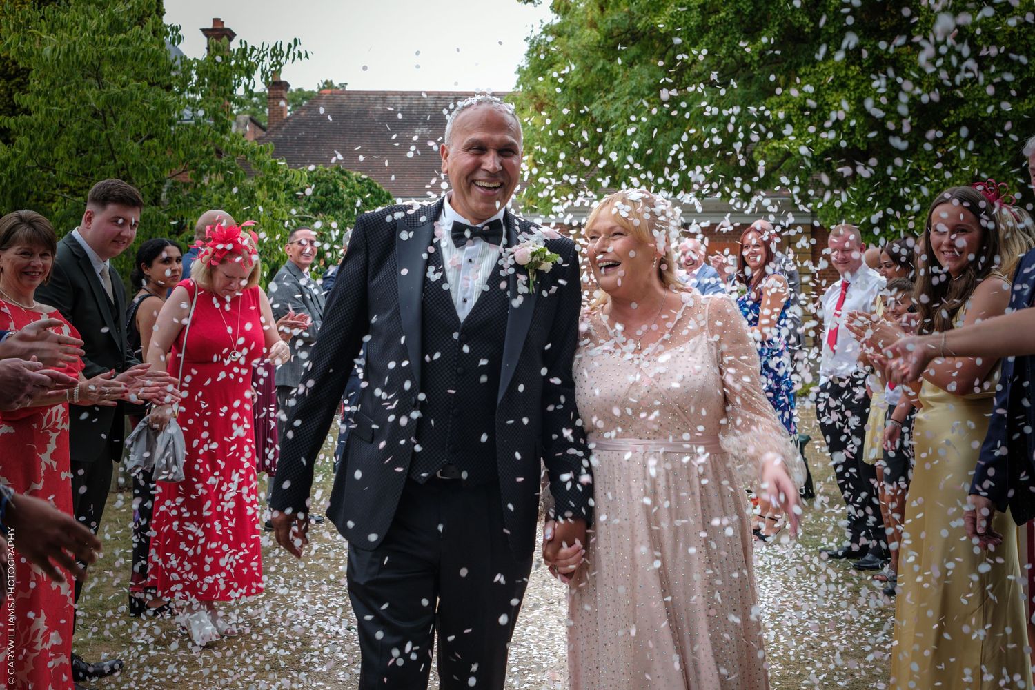 Newlyweds walk together under a shower of white confetti during an outdoor wedding celebration.