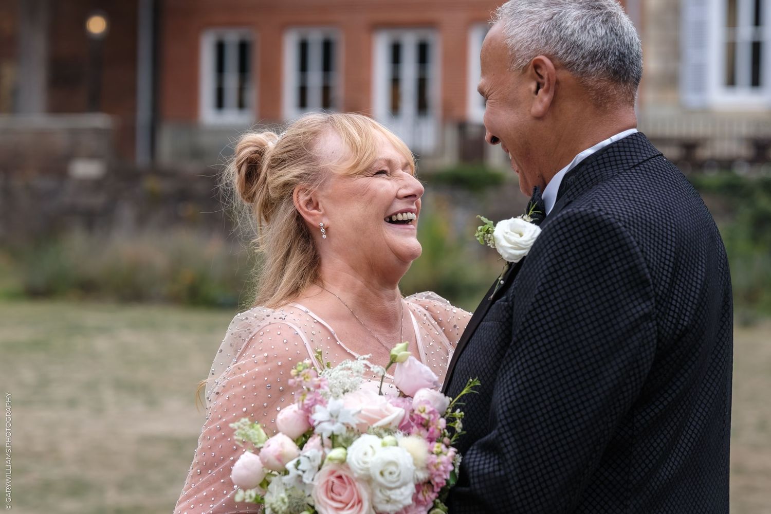 A happy couple shares a joyful moment at their wedding, with the bride holding a pink and white rose bouquet.