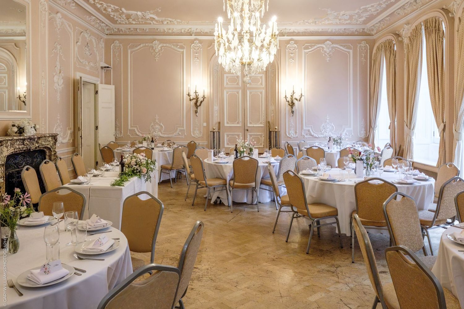 Elegant wedding reception ballroom with crystal chandeliers, ornate moldings, and tables set with white linens.