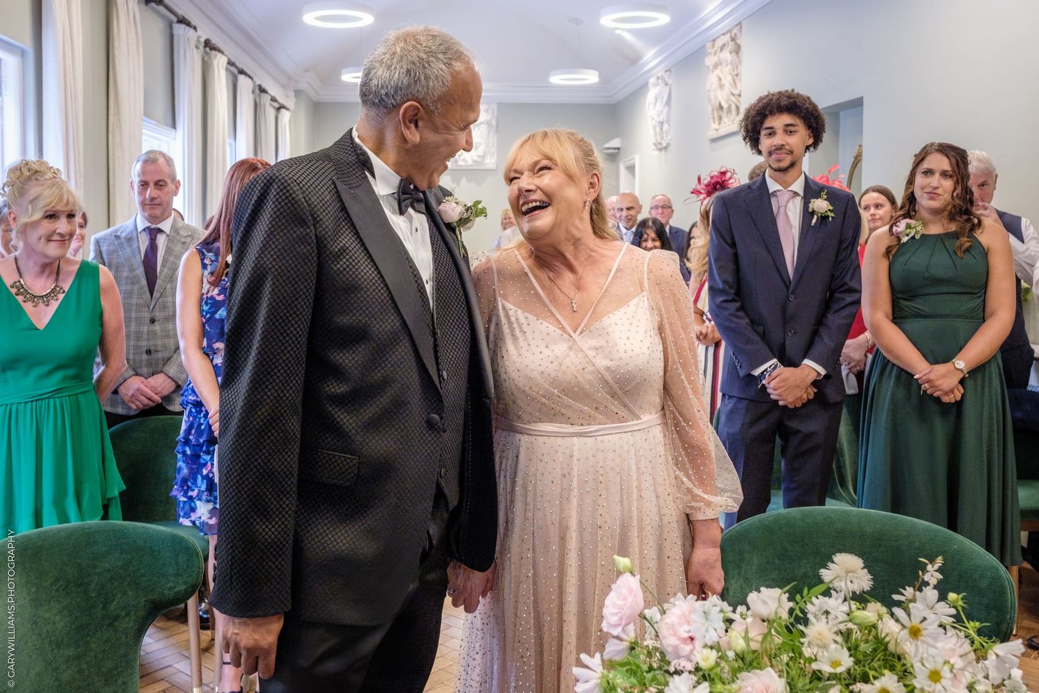 Stylishly dressed wedding guests stand in a grand hallway looking at a beautiful floral display at an elegant reception.