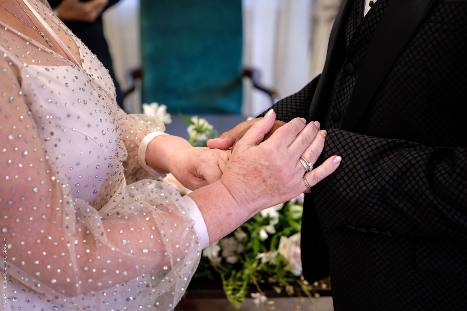 Wedding ceremony rings being exchanged in an outdoor garden setting with delicate pearl covered attire.