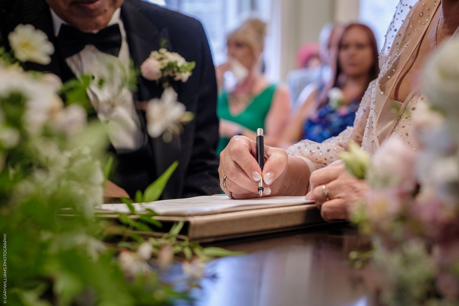 People signing documents at a table with pink cherry blossoms in the foreground during a celebration event.