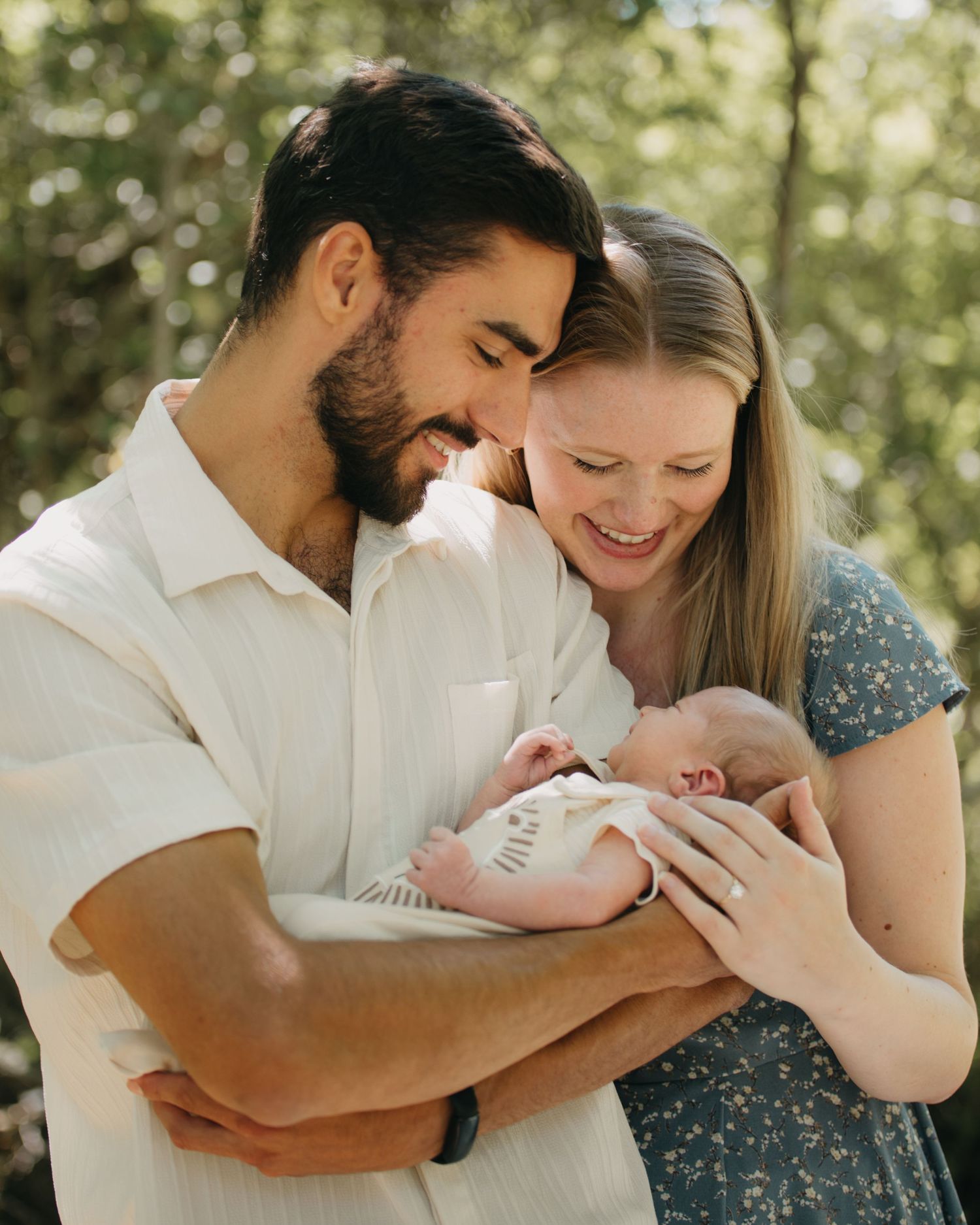 Joyful new parents smiling and holding their newborn baby close in a natural setting.