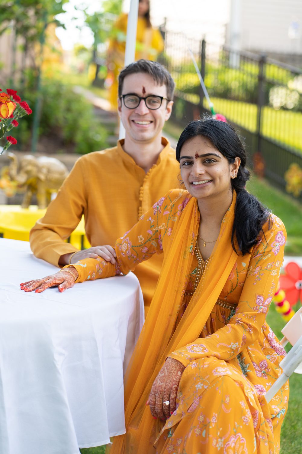 A couple in bright orange and white outfits smile together in a garden setting during an outdoor photo session Haldi Quad Cities Photography