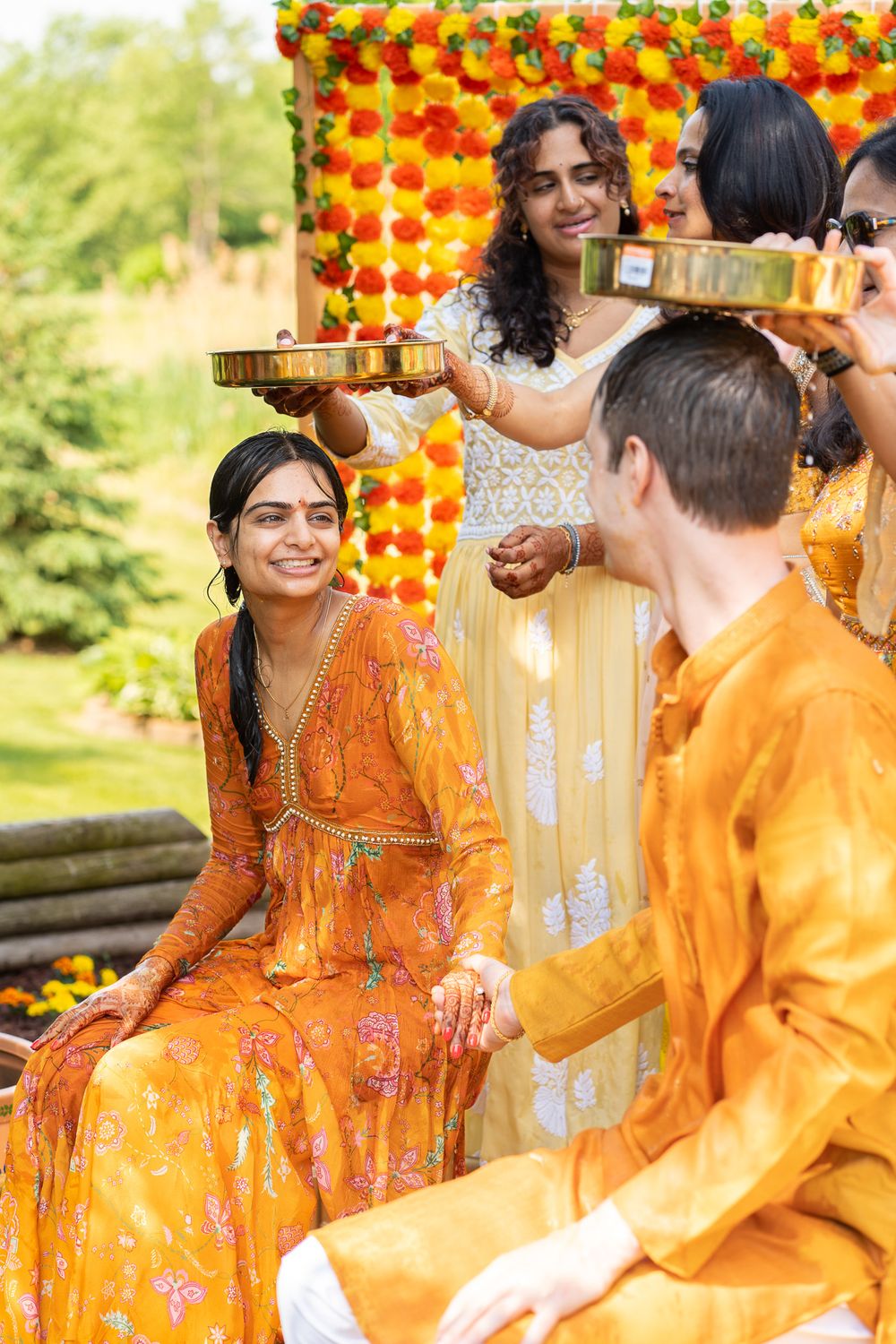 Group celebrates a traditional Indian ceremony outdoors bright yellow attire and orange flower decorations Haldi Quad Cities Photography