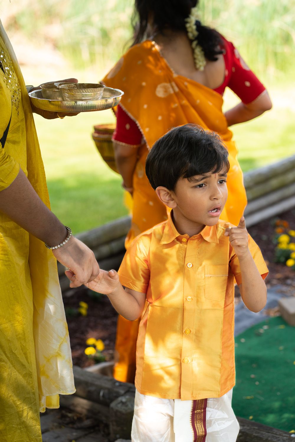 A small child wearing a bright orange shirt and white bottoms plays at an outdoor celebration event. Haldi Quad Cities Photography
