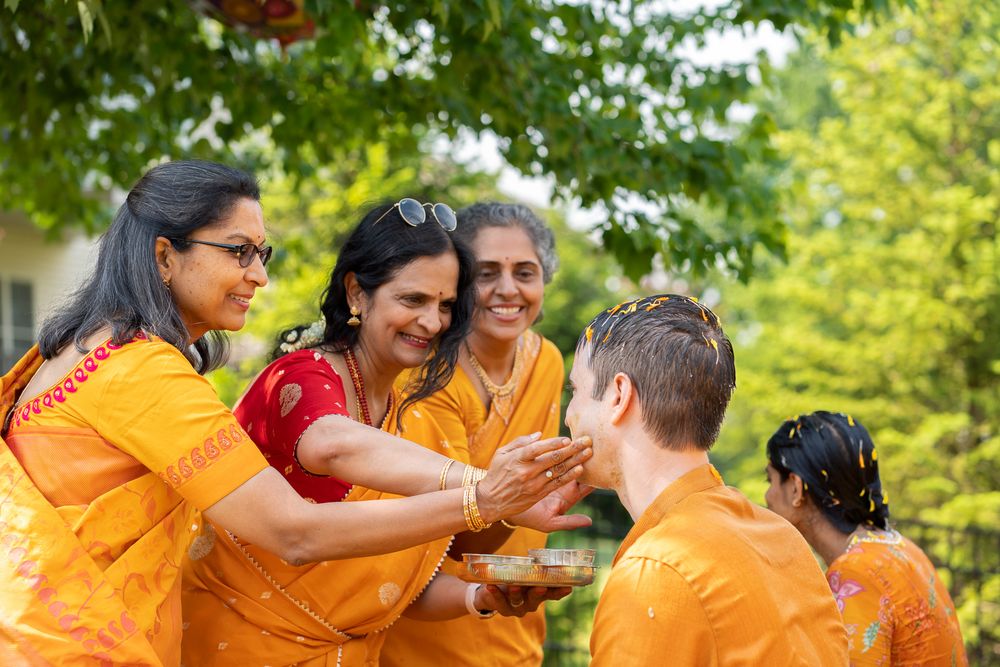 A group celebrates together outdoors in festive orange and red attire while enjoying a joyful moment in nature Haldi Quad Cities Photography